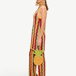 A person wears a Hazel Knit Dress, a sleeveless, floor-length crochet mini dress with a red, yellow, and green wavy pattern, carrying a small pineapple-shaped handbag.