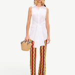A woman wearing a white sleeveless button-down shirt tied at the waist and colorful chevron-striped Ophelia Knit Pant, carrying a small woven handbag.