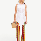 A woman wearing a white sleeveless button-down shirt tied at the waist and colorful chevron-striped Ophelia Knit Pant, carrying a small woven handbag.