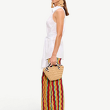 A person wearing a white sleeveless collared shirt and Ophelia Knit Pants featuring a colorful squiggle design, carrying a small woven handbag.