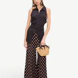 A model wears a black polka-dot Loch Sleeveless Crepe Button Up with matching wide-leg trousers and a small woven handbag.