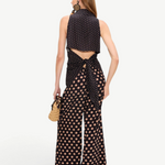 A person seen from behind wearing a tan polka-dot Loch Sleeveless Crepe Button Up with a tie-waist and matching wide-leg trousers for an elegant look.