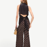 A person seen from behind wearing a tan polka-dot Loch Sleeveless Crepe Button Up with a tie-waist and matching wide-leg trousers for an elegant look.