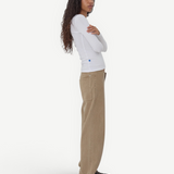 Model wearing KABE SHOP INC relaxed fit tan denim Sport Jean with a white long-sleeve top against a grey background