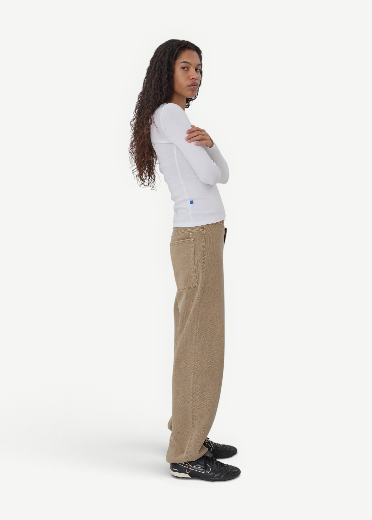 Model wearing KABE SHOP INC relaxed fit tan denim Sport Jean with a white long-sleeve top against a grey background