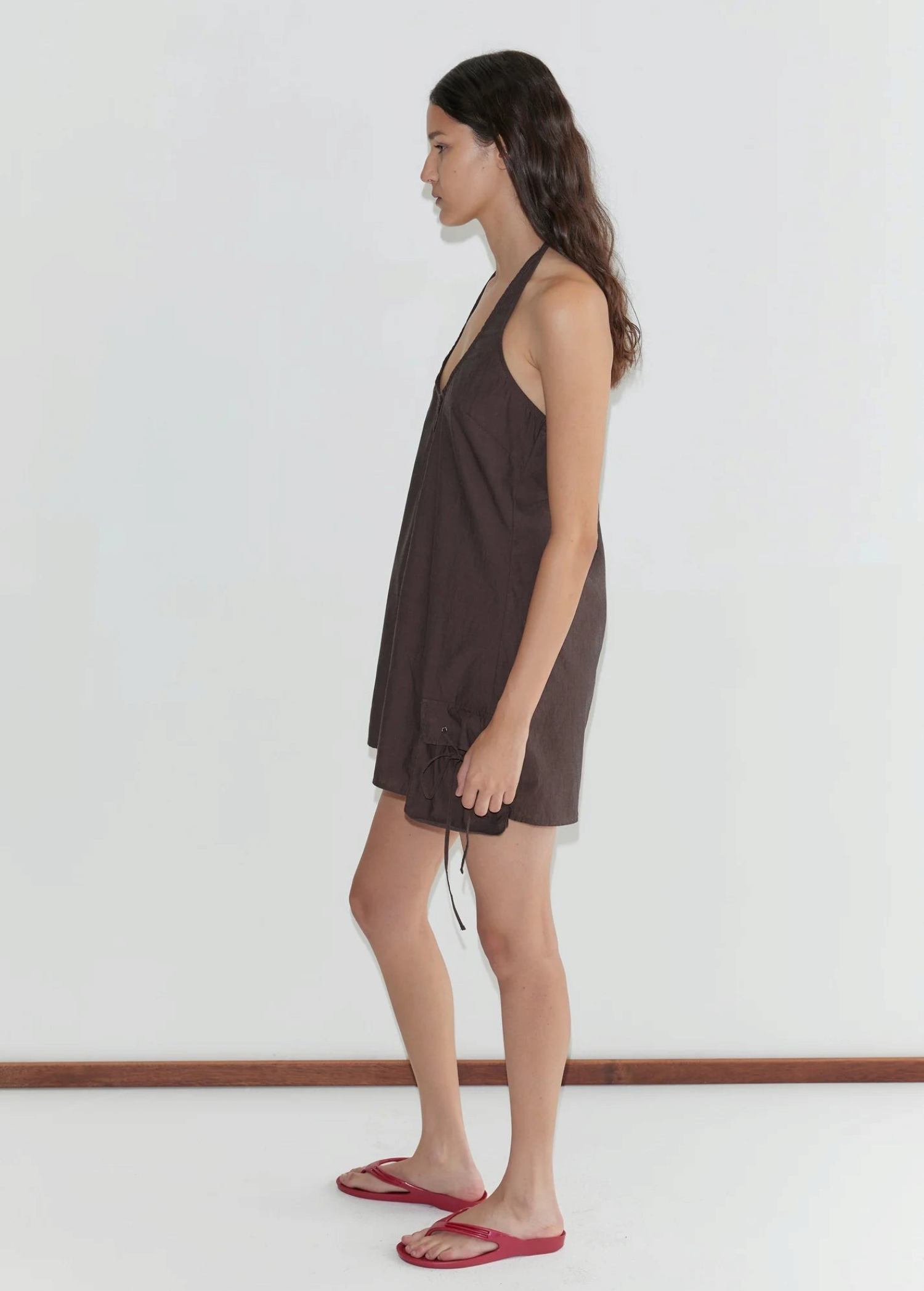 Model wearing a dark brown Deiji Studios pocket halter dress with scalloped details and eyelet pockets from KABE SHOP INC