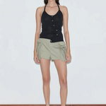 A woman wearing a Cross Top with an asymmetrical button front and light green cargo shorts.