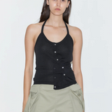 A person wears a Cross Top featuring a fitted knit halter design with an asymmetrical button-front closure and adjustable tie straps, paired with olive green shorts.
