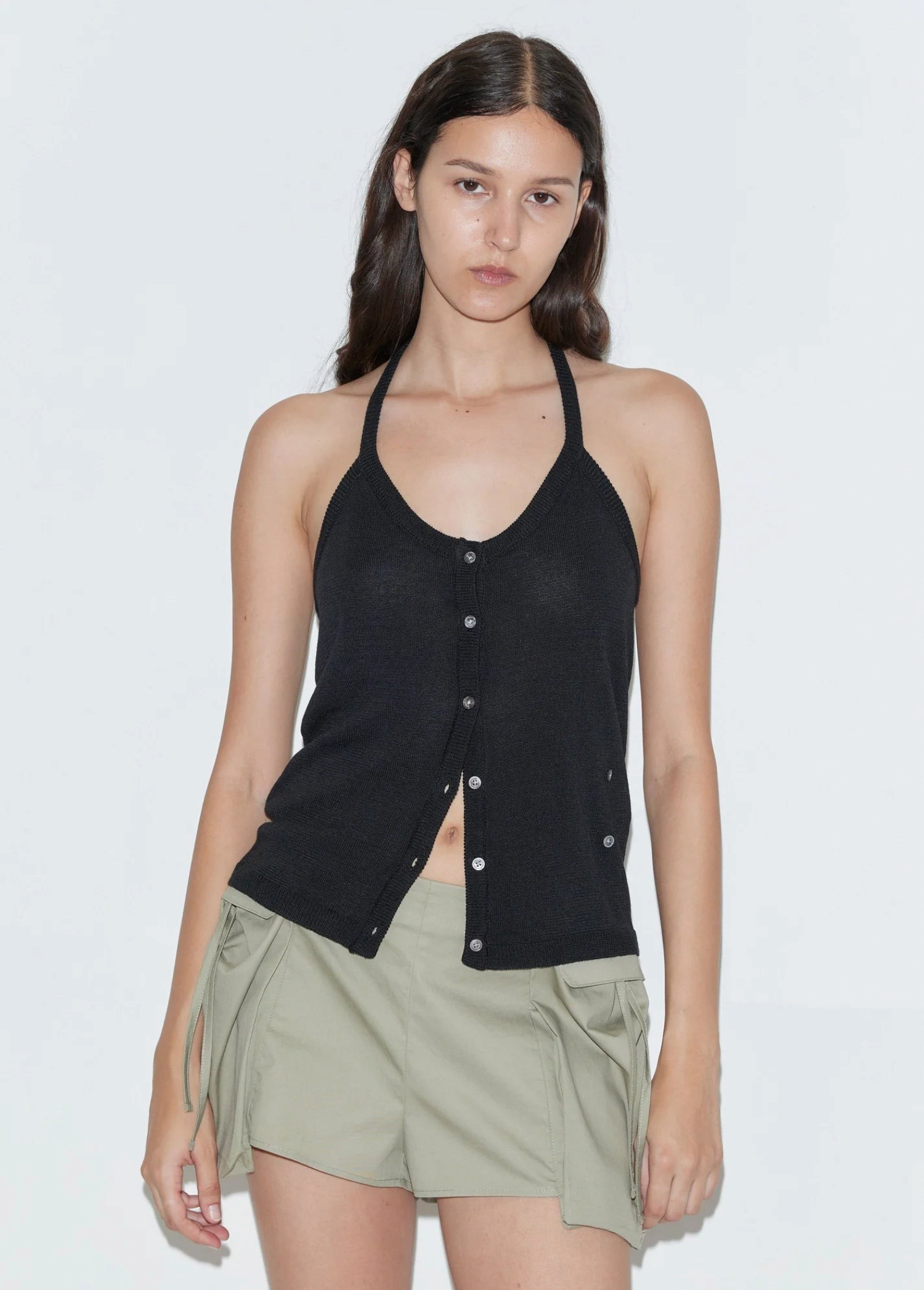 A person wears a black Cross Top featuring a fitted knit halter silhouette, deep V-neckline, button-down front, and crossover hem.