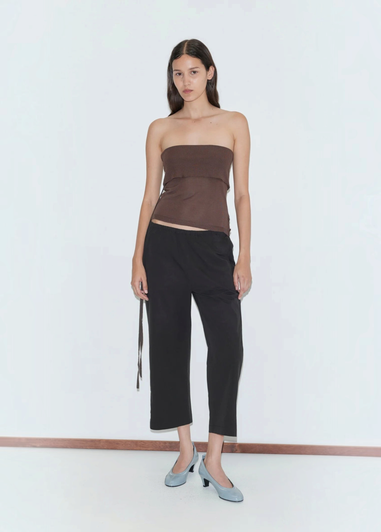 A person wearing a brown tube top, black cropped Capri Pant, and light blue kitten heels, styled for a relaxed look.