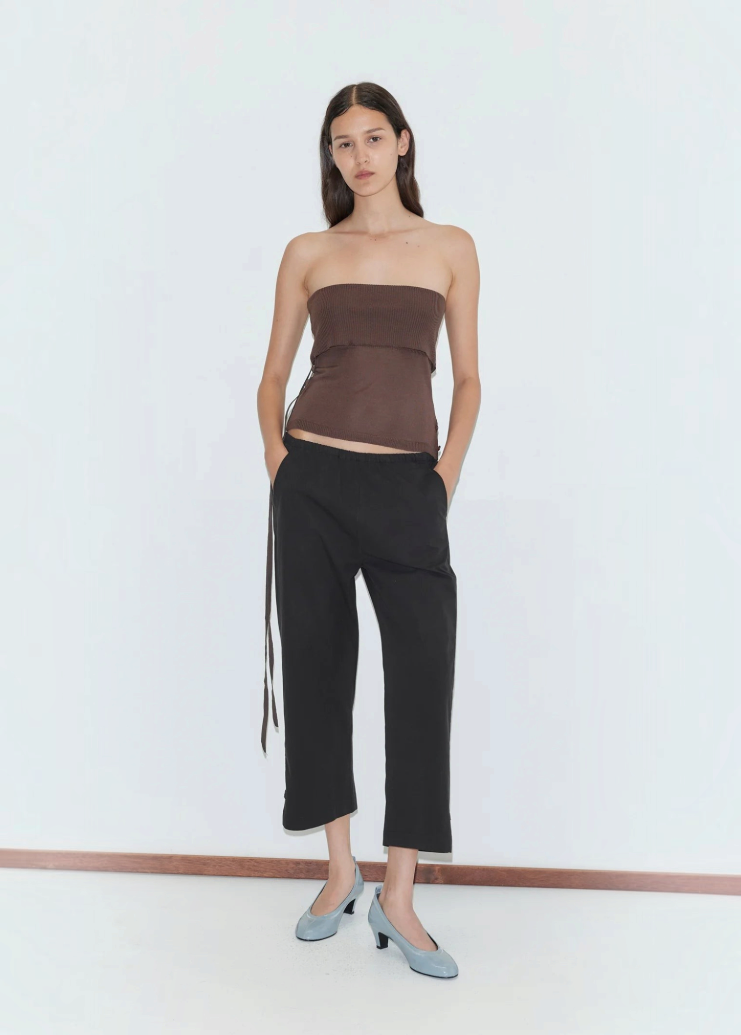 A woman wears a brown strapless top and relaxed style black Capri Pant with light blue low-heeled pumps.