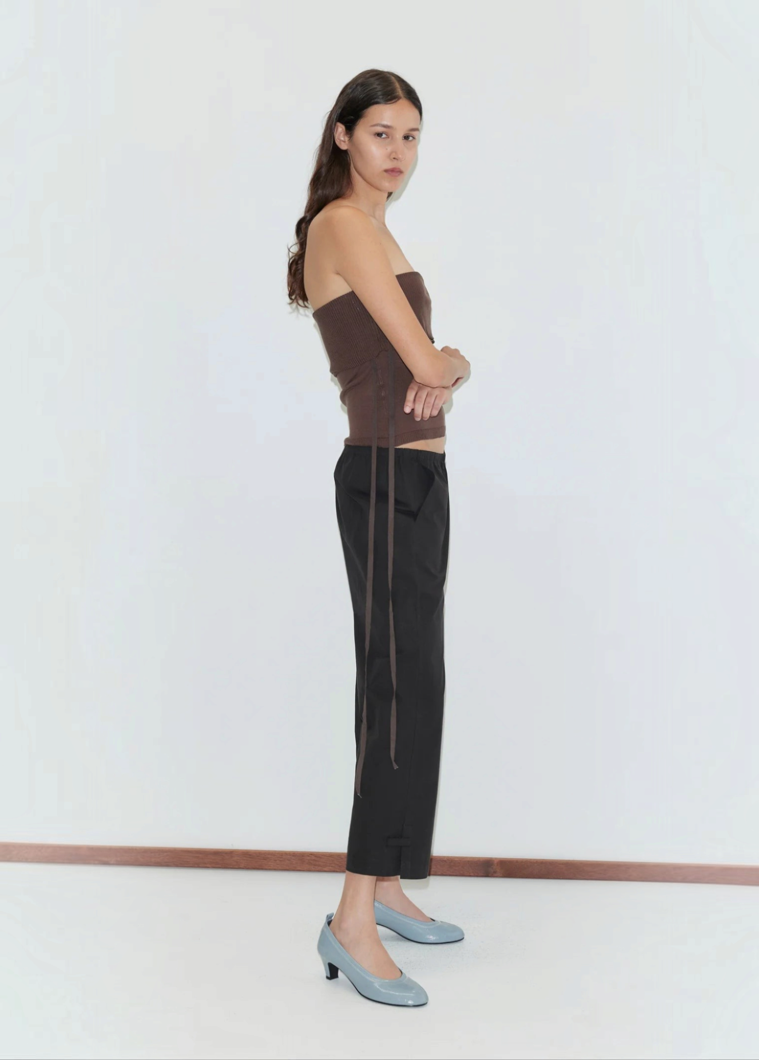 A person wearing a brown strapless top, black Deiji Studios Capri Pant, and light blue kitten heels in a relaxed style.