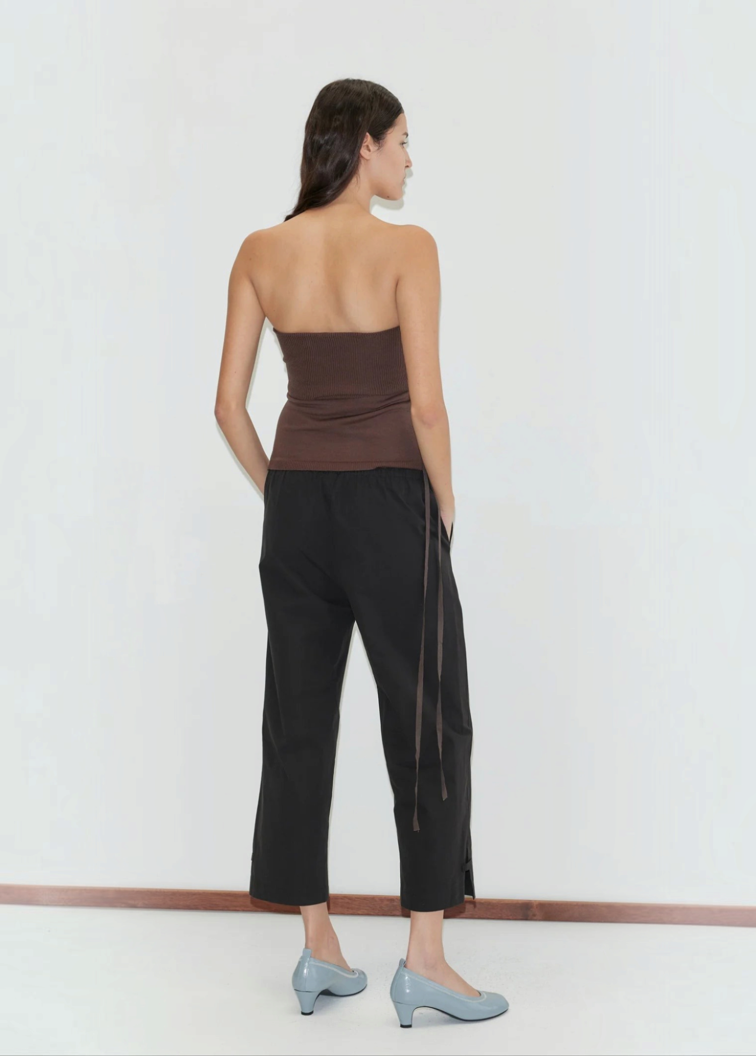 A person seen from behind, wearing a brown tube top, black Deiji Studios Capri Pant with side ties, and light blue block-heeled shoes.
