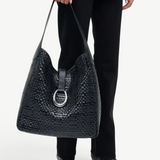 KABE SHOP INC Maya hobo bag in black woven leather with a silver ring clasp held by a person in a two-tone sweater.
