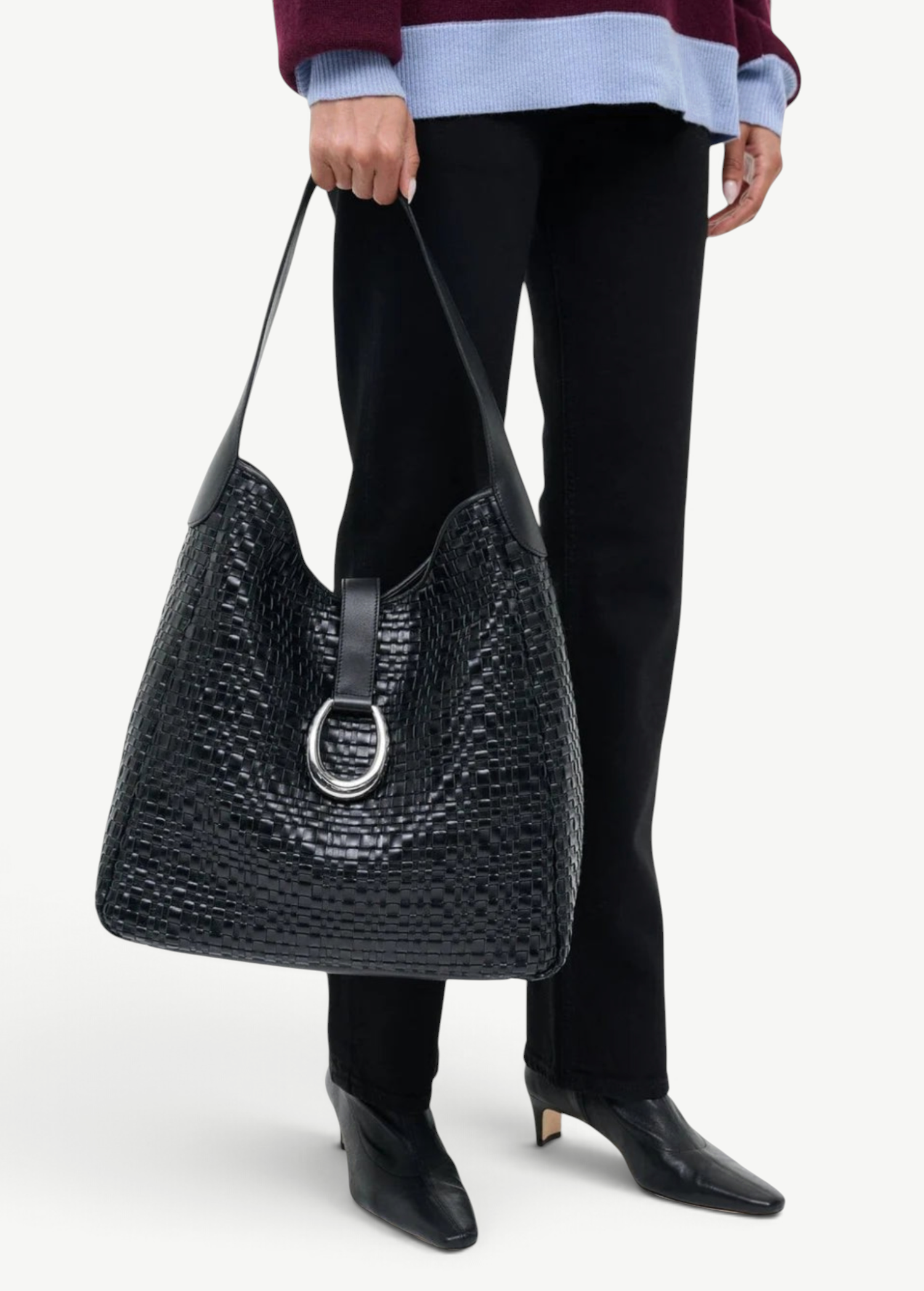 KABE SHOP INC Maya hobo bag in black woven leather with a silver ring clasp held by a person in a two-tone sweater.