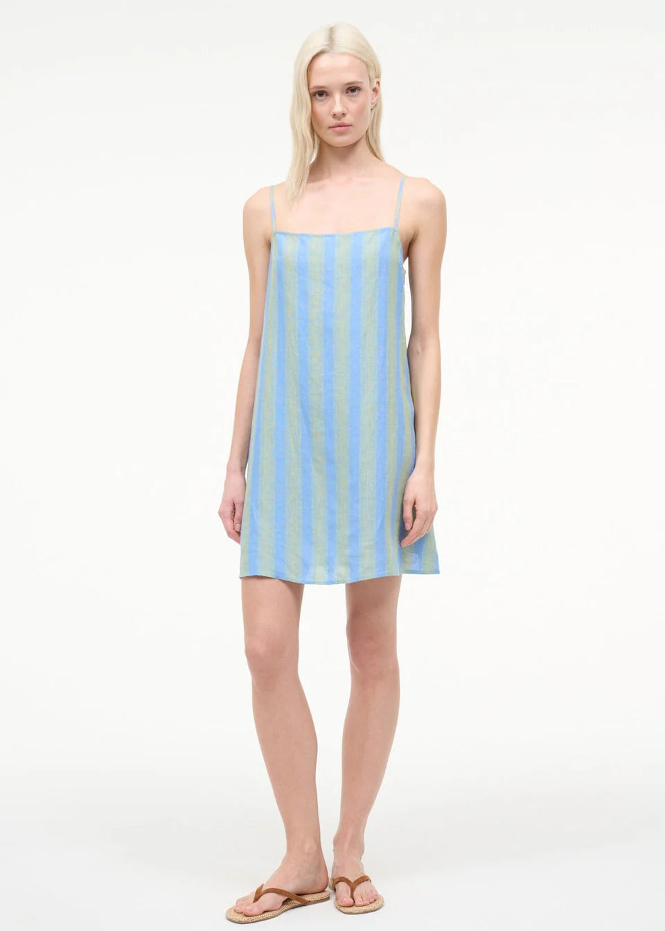 A model wearing the Laura Mini Dress, a sleeveless, blue and green striped mini dress with spaghetti straps, perfect for warm-weather dressing.