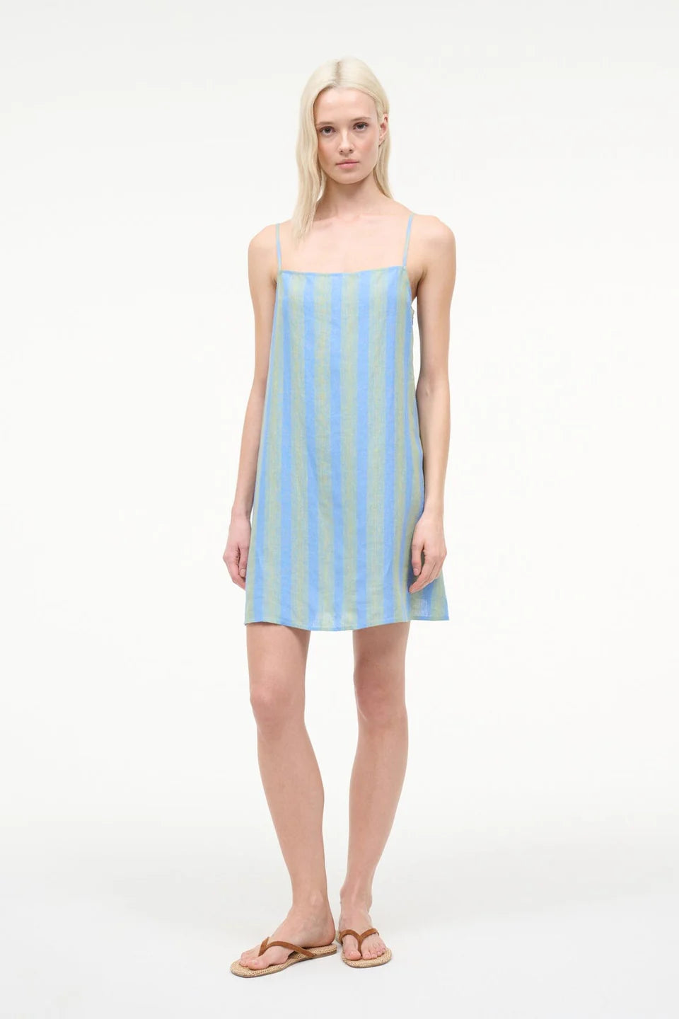 A model wearing the Laura Mini Dress, a sleeveless, blue and green striped mini dress with spaghetti straps, perfect for warm-weather dressing.
