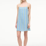 A model wearing the Laura Mini Dress, a sleeveless, blue and green striped mini dress with spaghetti straps, perfect for warm-weather dressing.
