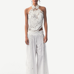 Model wearing KABE SHOP INC Menorca white cotton trousers with intricate lace detailing and a matching lace halter top.
