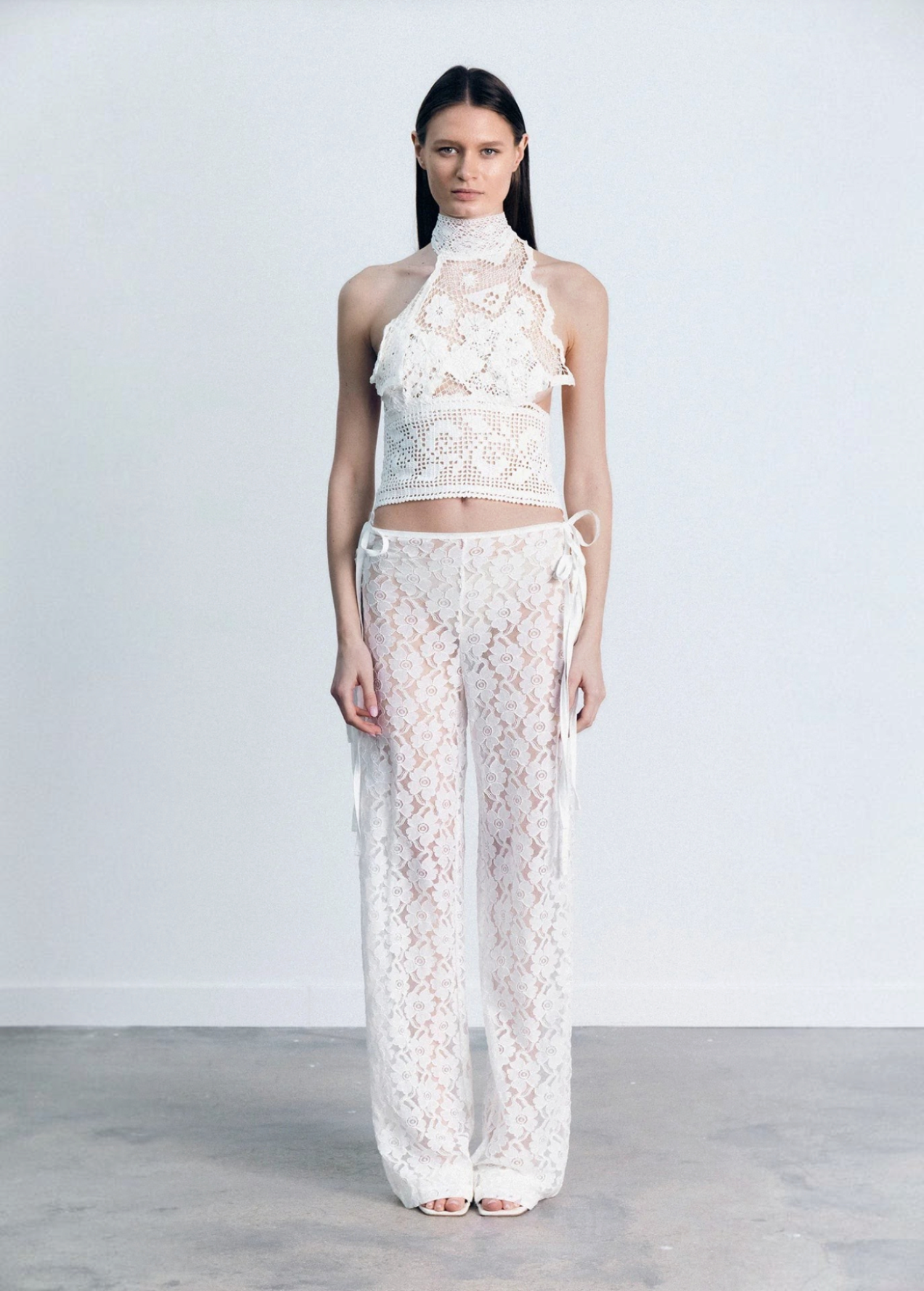 Model wearing KABE SHOP INC white lace trousers with a handkerchief-inspired waistband and matching lace halter top.