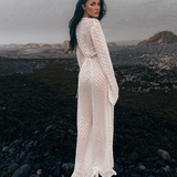 Model wearing a KABE SHOP INC Mirror Dress in sheer white fabric with silver embellishments on a rocky beach