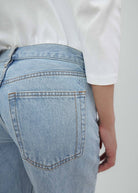 A person is wearing light blue Everyday Jeans and a white long-sleeve shirt, shown from the back and waist down, with one hand resting by their side. The versatile Everyday Jeans feature visible stitching, a relaxed silhouette, and classic back pockets.