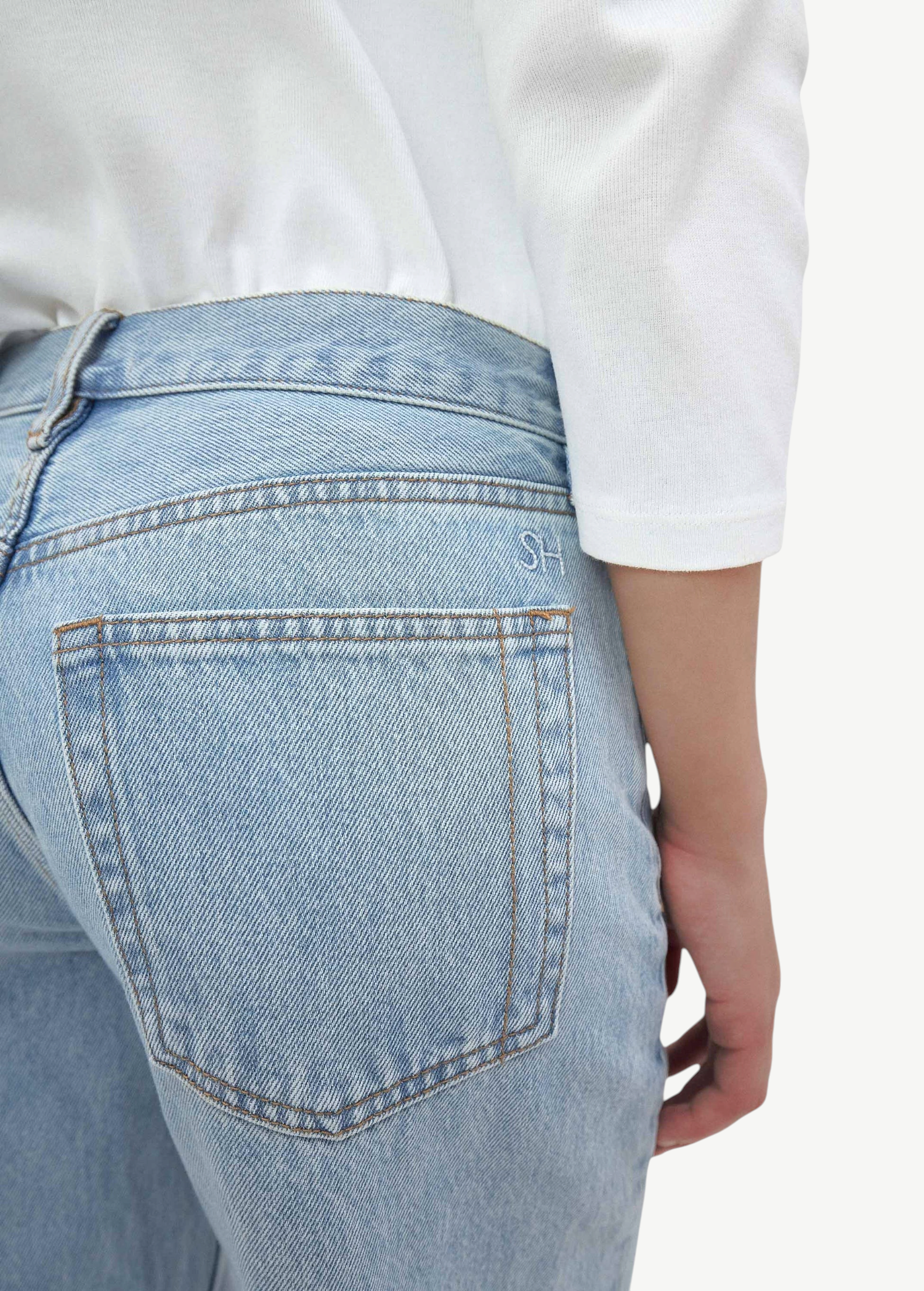 A person is wearing light blue Everyday Jeans and a white long-sleeve shirt, shown from the back and waist down, with one hand resting by their side. The versatile Everyday Jeans feature visible stitching, a relaxed silhouette, and classic back pockets.