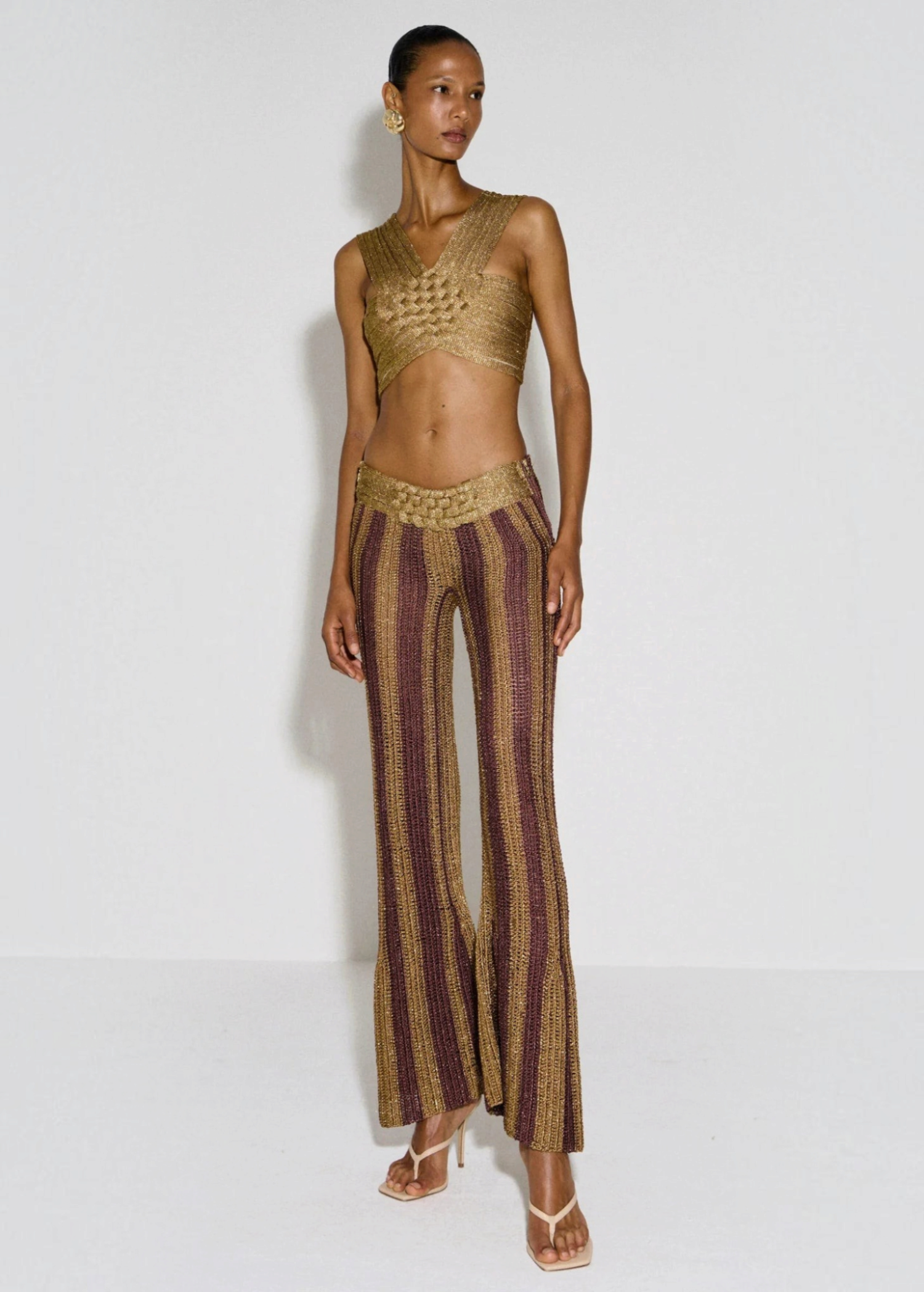 Model wearing KABE SHOP INC Cher Set featuring a gold metallic woven crop top and matching striped flared trousers.