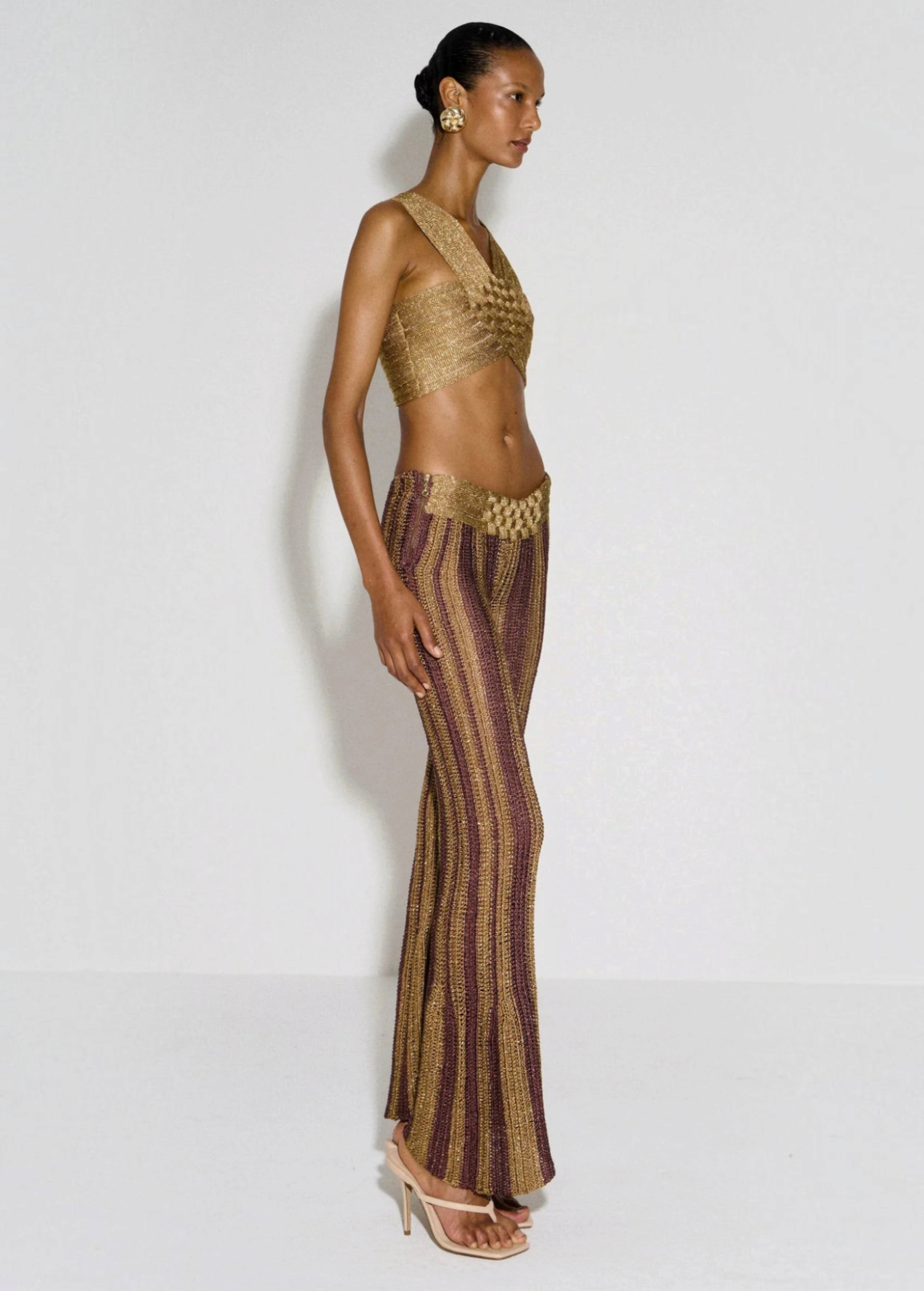 Model wearing KABE SHOP INC Cher Set featuring a metallic gold crop top and striped burgundy and gold flared trousers.