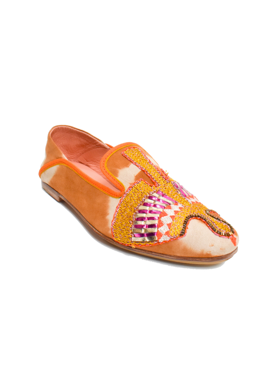 The Anzu Moccasin is an orange and tan slip-on featuring pink, yellow, and gold hand-embroidered patterns on the upper. With a flat sole and rounded toe, this sustainable shoe is inspired by the classic moccasin and is displayed on a white background.