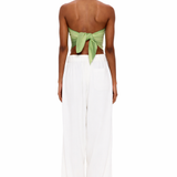 A person stands facing away, wearing The Triangle Top—a green back-tied bandeau inspired by traditional Moroccan weaving—and loose white pants, set against a plain white background.