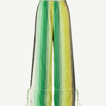 The Parachute Pant features a wide-leg silhouette with vertical green, yellow, and white stripes, expertly crafted from handwoven cotton to highlight exquisite Moroccan craftsmanship. Designed with an elastic waistband and adjustable drawstrings at the ankles, these pants are showcased against a white background.