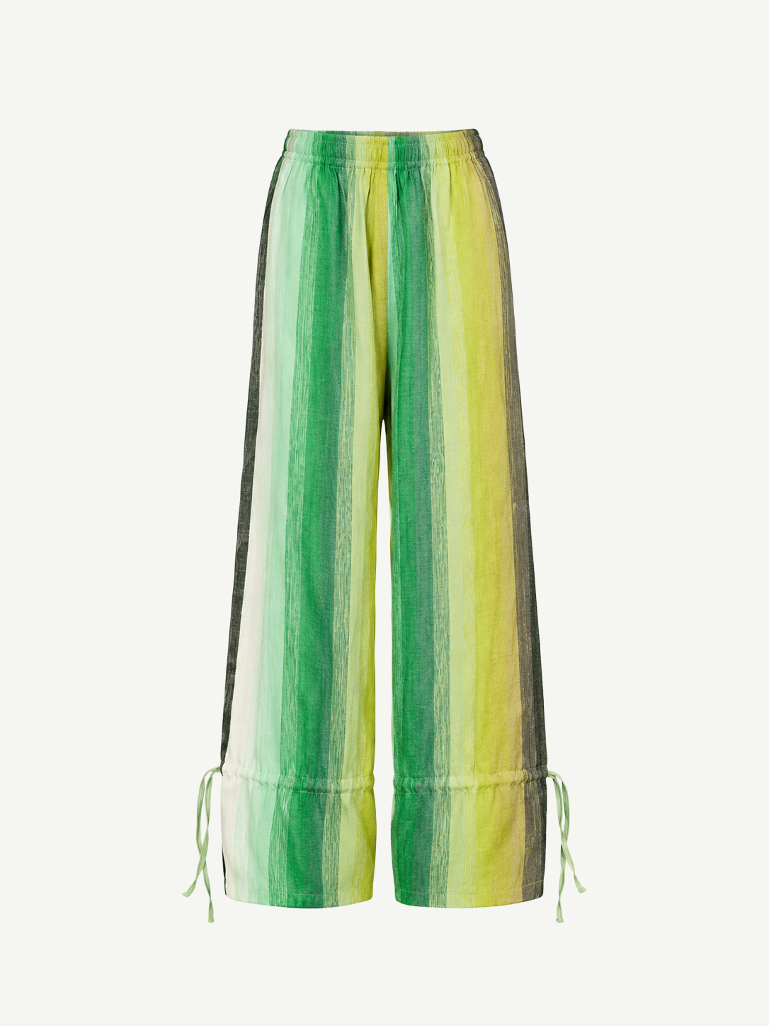 The Parachute Pant features a wide-leg silhouette with vertical green, yellow, and white stripes, expertly crafted from handwoven cotton to highlight exquisite Moroccan craftsmanship. Designed with an elastic waistband and adjustable drawstrings at the ankles, these pants are showcased against a white background.