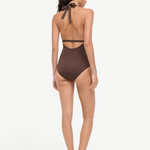 A woman viewed from behind wearing a brown La Jolla Swimwear one-piece swimsuit with a halter-style cut-out back and black flat sandals, perfect for vacation dressing.