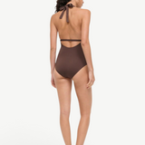 A woman viewed from behind wearing a brown La Jolla Swimwear one-piece swimsuit with a halter-style cut-out back and black flat sandals, perfect for vacation dressing.