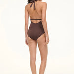 A woman viewed from behind wearing a brown La Jolla Swimwear one-piece swimsuit with a halter-style cut-out back and black flat sandals, perfect for vacation dressing.