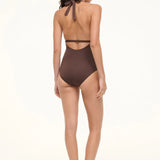 A woman viewed from behind wearing a brown La Jolla Swimwear one-piece swimsuit with a halter-style cut-out back and black flat sandals, perfect for vacation dressing.