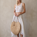 KABE SHOP INC large palm leaf shaped raffia bag with brown leather handles held by a blonde model in white summer wear