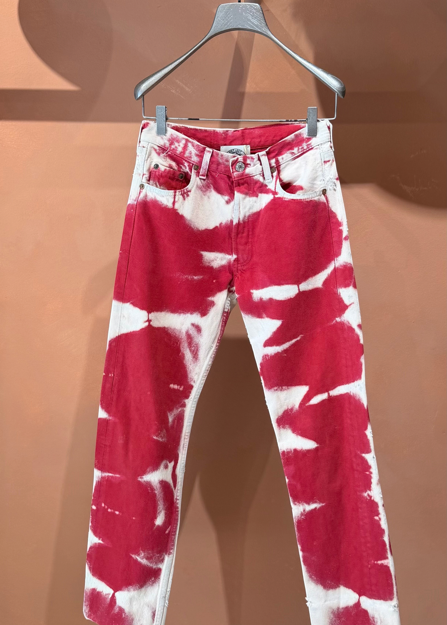 Red and white Tie Dye Jeans in a vintage style on a clothes hanger.