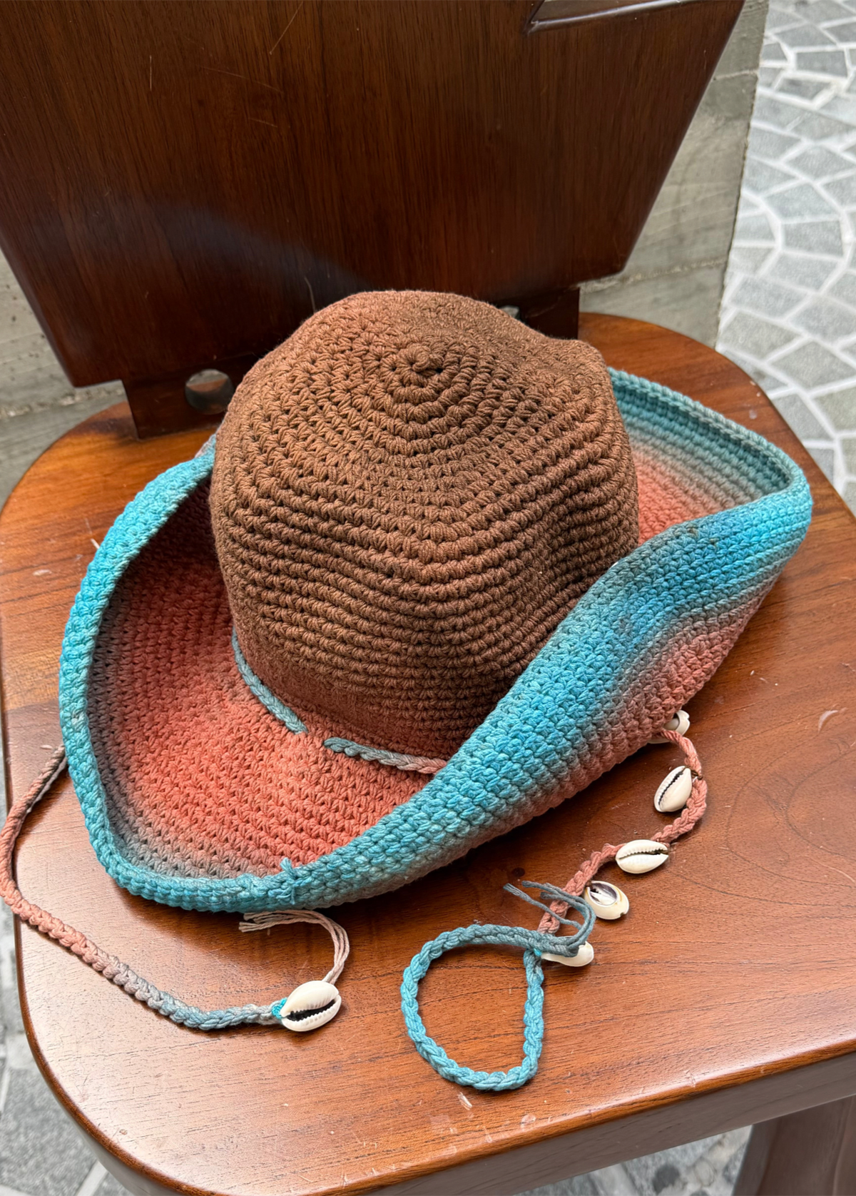 KABE SHOP INC Wika crochet tie-dye hat in brown, orange, and blue with seashell accents on a wooden chair