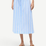 The Shore Skirt is a light blue and white vertical-striped stretch poplin midi skirt featuring a gathered elastic paper-bag waist with a drawstring.