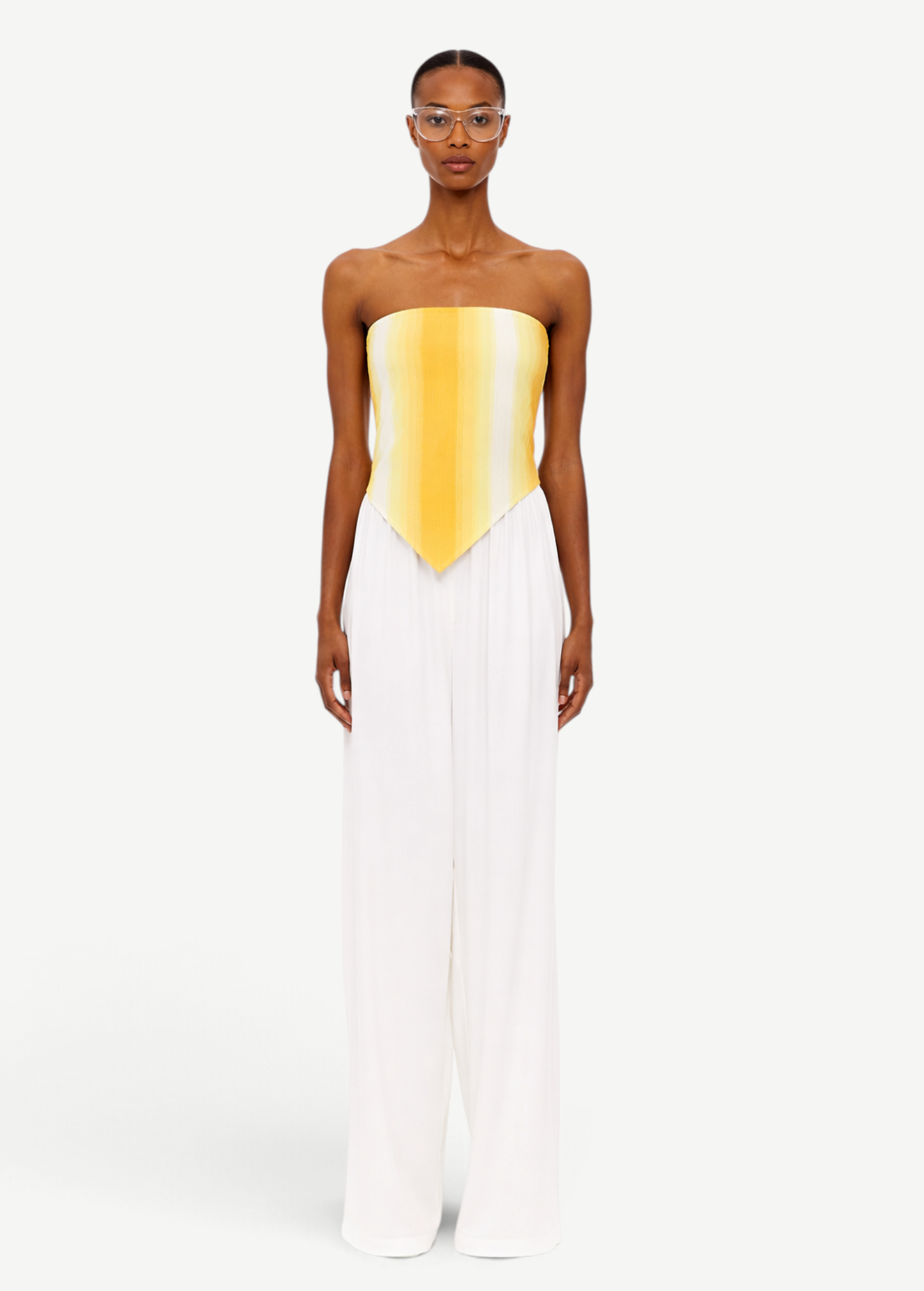 Wearing The Triangle Top—a strapless, yellow-to-white gradient piece crafted with sustainable Marrakech fashion techniques—and high-waisted, wide-leg white pants, the person stands facing forward against a plain white background.