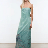 A model wears the Amara Dress, a strapless, light green midi with a sheer overlay featuring a printed coastal scene and scattered rhinestones.
