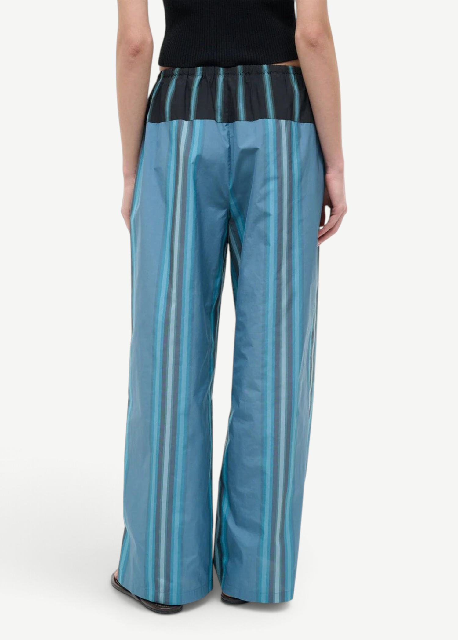 Back view of the Mateo Pant, featuring wide-leg trousers in blue and teal vertical stripes with a black elastic waistband.