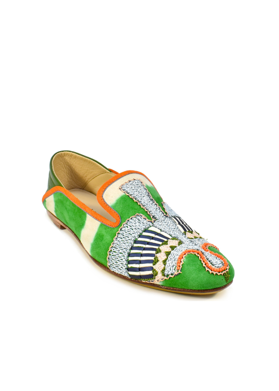The Anzu Moccasin is a vibrant babouche-style loafer crafted from green, orange, and white suede, adorned with intricate beaded details and hand-embroidered moccasin patterns on the front and sides.