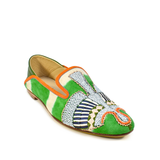 The Anzu Moccasin is a vibrant babouche-style loafer crafted from green, orange, and white suede, adorned with intricate beaded details and hand-embroidered moccasin patterns on the front and sides.