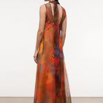 A woman wears an elegant, floor-length Albee Dress in a sleeveless, sheer, multicolor floral print with a high neck and tie detail at the back.