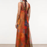 A woman wears an elegant, floor-length Albee Dress in a sleeveless, sheer, multicolor floral print with a high neck and tie detail at the back.