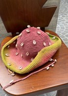 KABE SHOP INC crochet tie-dye hat in pink and green with decorative seashells on a wooden chair