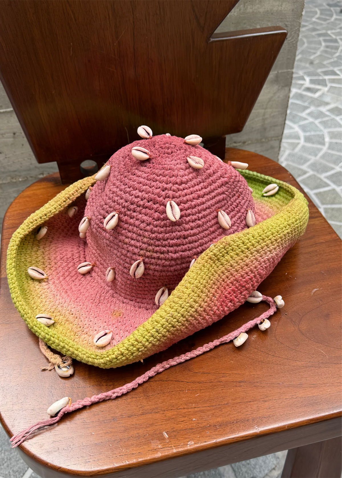 KABE SHOP INC crochet tie-dye hat in pink and green with decorative seashells on a wooden chair